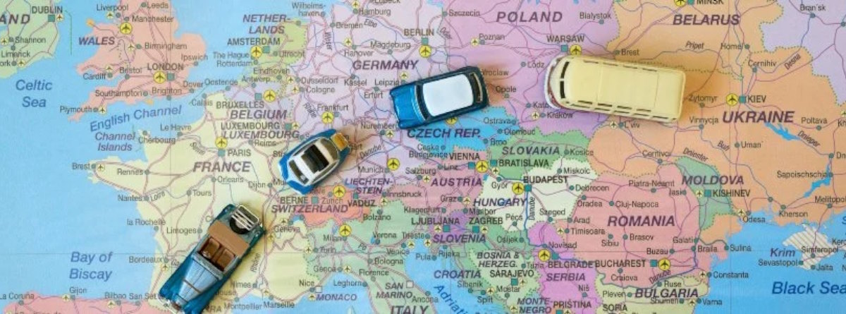 articulo Vista superior de un mapa político de Europa con varios coches en miniatura y una autocaravana de juguete colocados sobre distintos países para simbolizar viajes por carretera.